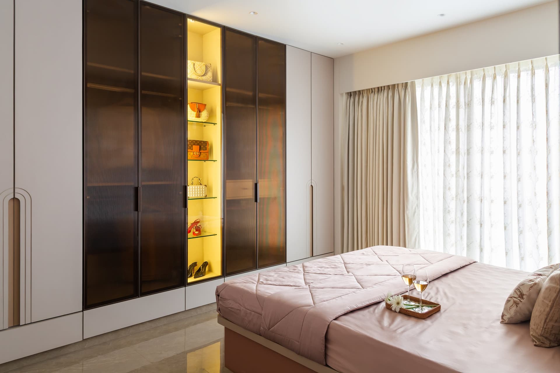 The wardrobe wall, with smoked glass fronts and an amber-lit display column that turns storage into a dressing composition